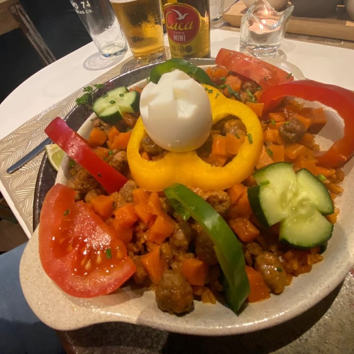 Gambian jollof rice: A vibrant bed of rice rice with yellow, red, and green peppers, cucumber, and a hard-boiled egg