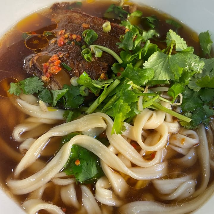 Huge bowl of spicy Chinese broth full of fresh noodles, coriander and pork belly