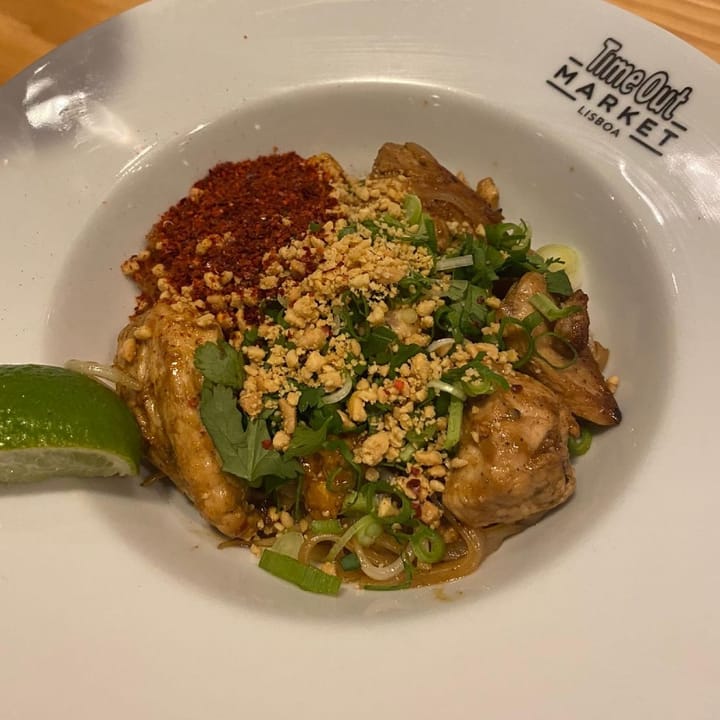A bowl of chicken pad thai loaded with peanuts, coriander, chilli and lime wedge