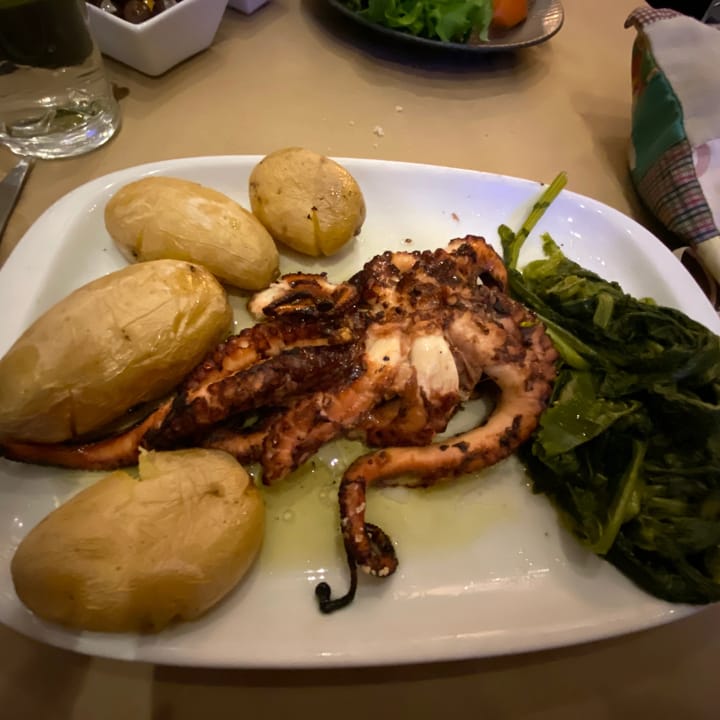 A plate of grilled octopus with boiled potatoes and wilted spinach, a classic Portuguese dish