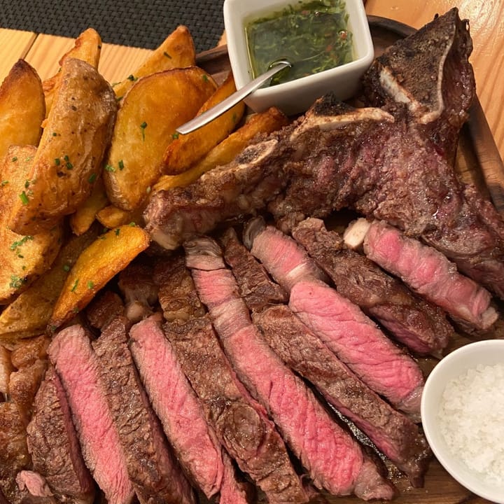 A perfectly medium rare chuleton or prime rib steak served with potato wedges and chimmichurri